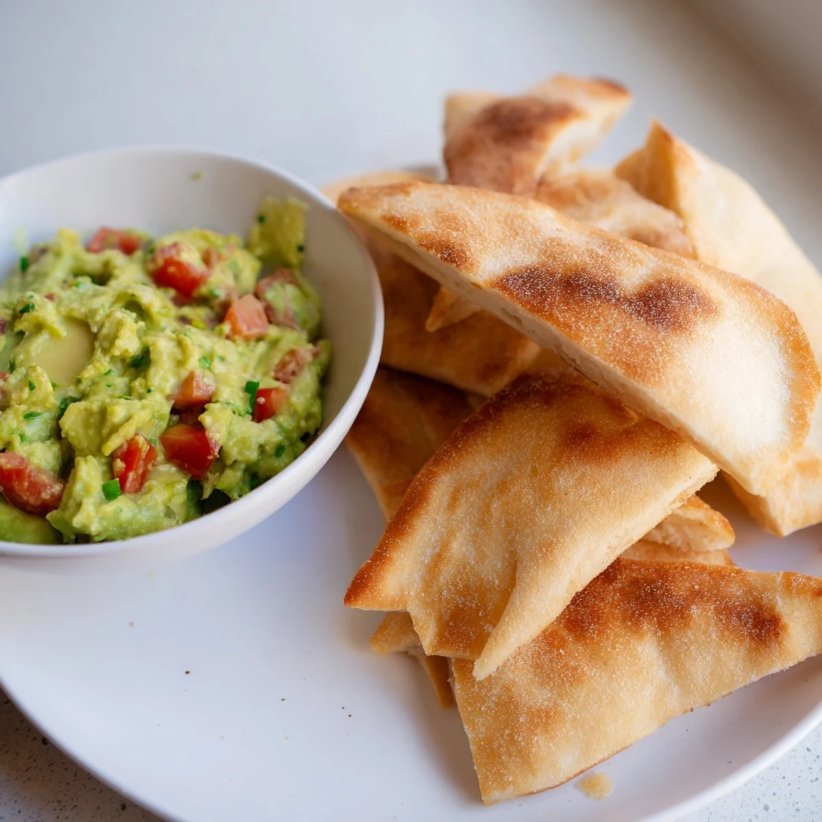 Golden, crunchy pita chips ready to be scooped into the vibrant, creamy guacamole bowl.