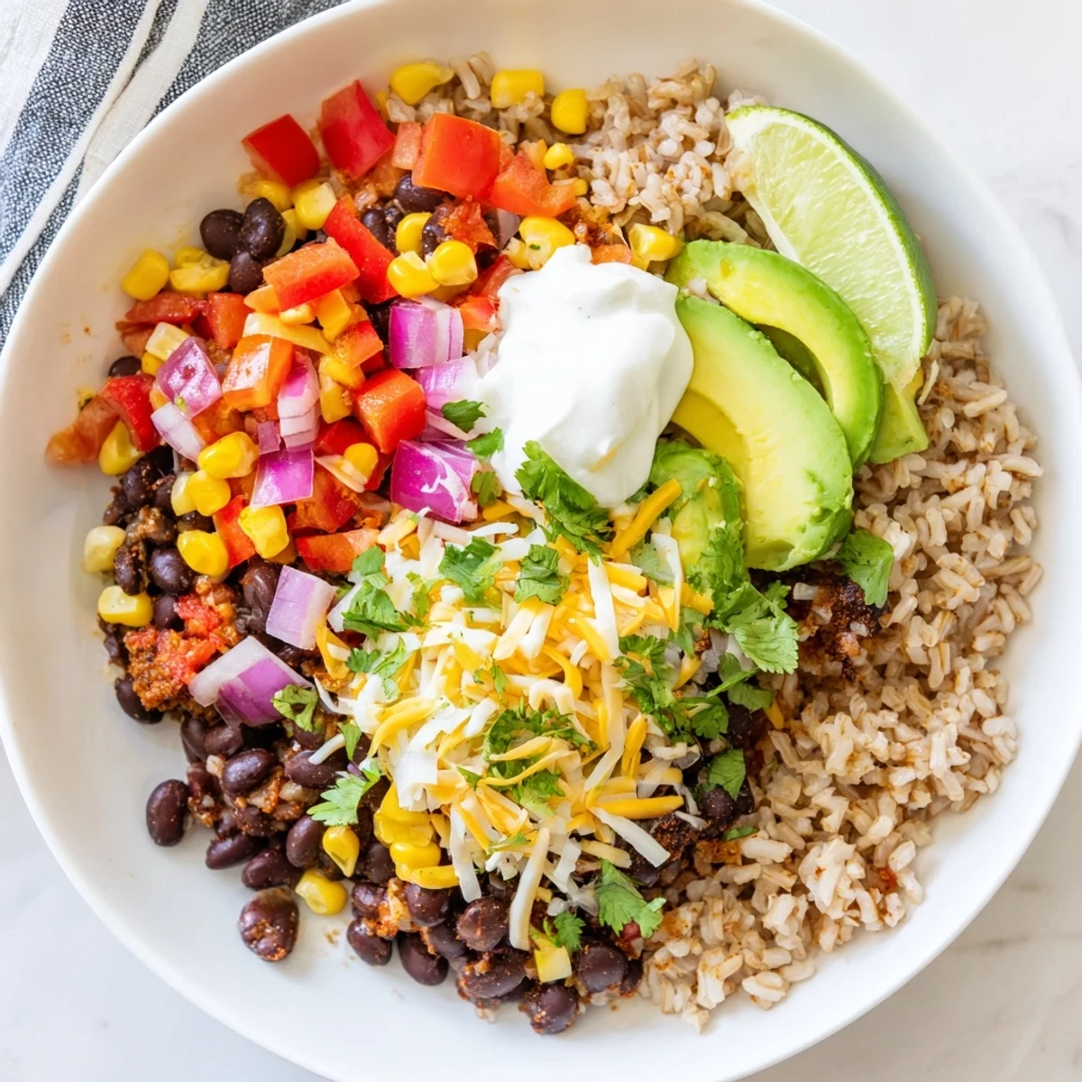 A vibrant Brown Rice Burrito Bowl with fluffy rice, hearty black beans, diced peppers, corn, and creamy avocado slices.  