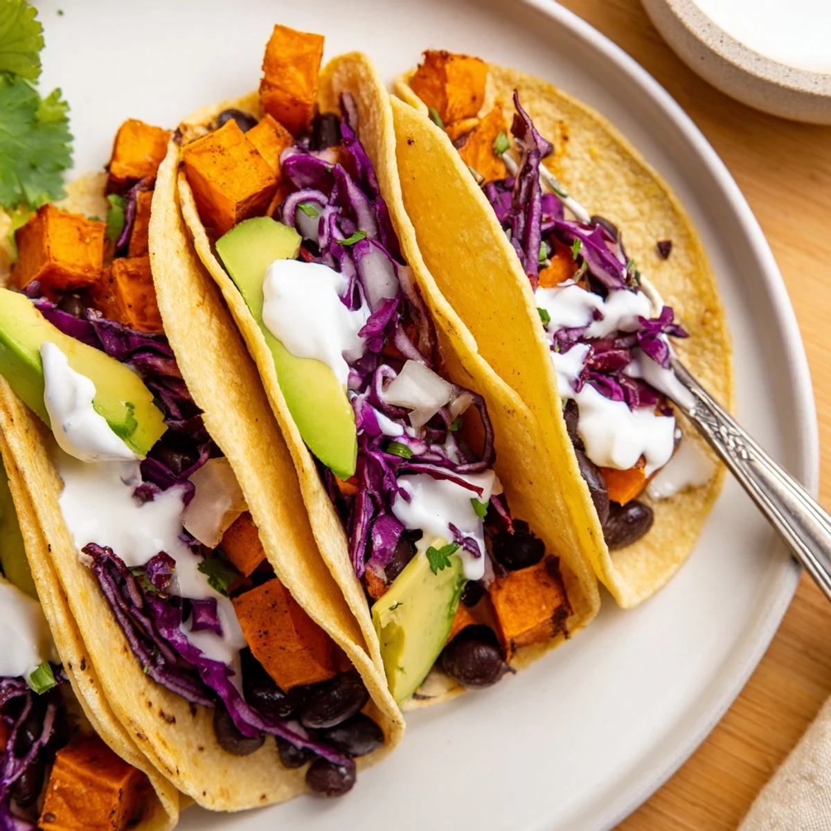 Hearty roasted sweet potatoes and black beans fill golden corn tortillas, topped with creamy avocado and shredded cabbage.  