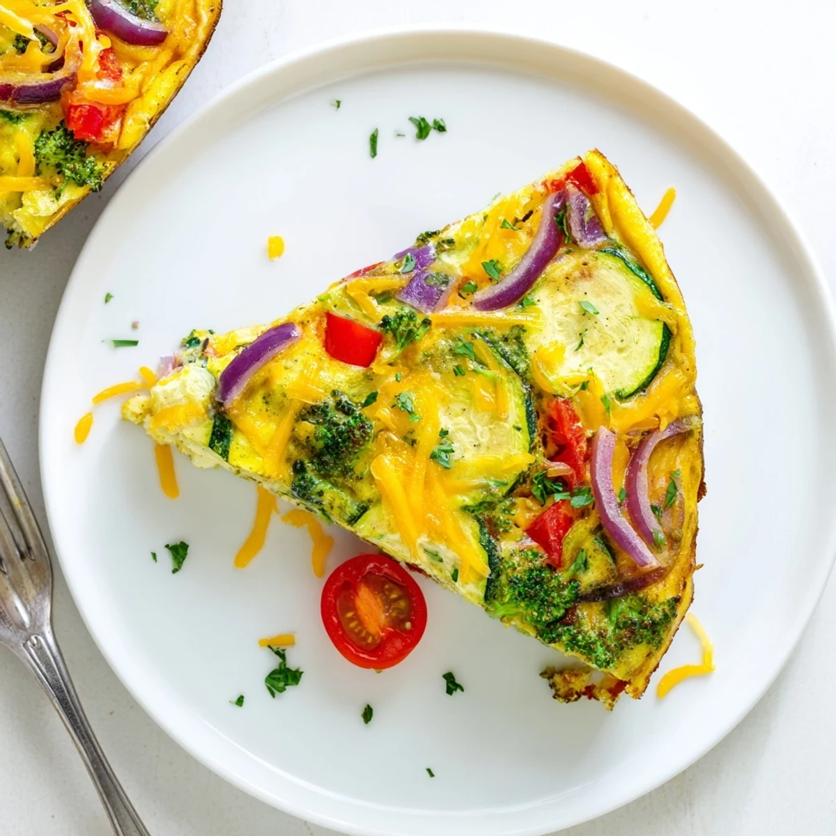 A freshly baked vegetable frittata in a skillet, topped with melted cheese and vibrant red bell peppers, zucchini, and cherry tomatoes.  