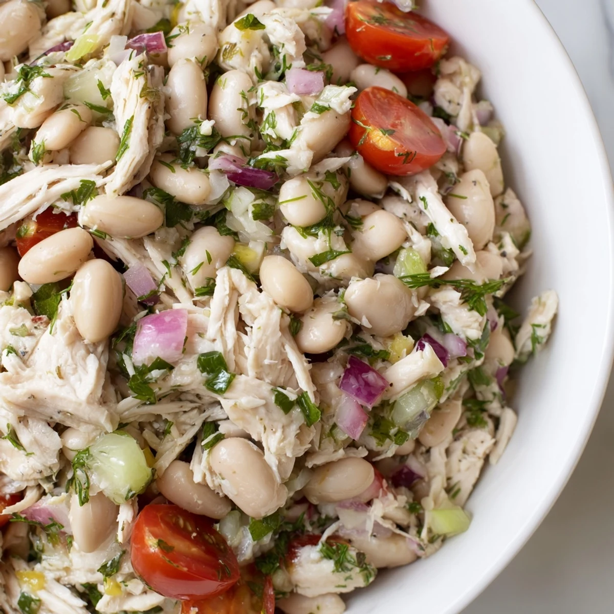 Close-up of Lemony White Bean Chicken Salad featuring fresh dill and parsley, served on a plate with cherry tomatoes and red onion.