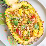 Vibrant Pineapple Fried Rice served inside a hollowed pineapple shell, garnished with cilantro and lime wedges for a tropical Thai-inspired presentation.