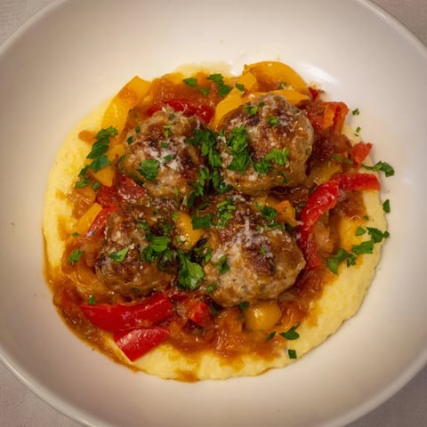 Herb-Cozy Skillet Sausage and Peppers with creamy polenta, a hearty, steaming, Italian-inspired dish on a plate.