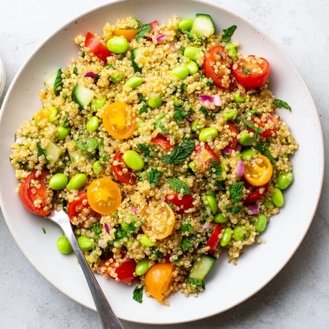 A vibrant bowl of Edamame and Quinoa Salad filled with red bell peppers and fresh herbs.