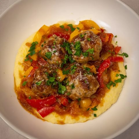 Herb-Cozy Skillet Sausage and Peppers with creamy polenta, a hearty, steaming, Italian-inspired dish on a plate.