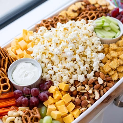 A tempting movie night munchie board overflowing with popcorn, pretzels, and fresh, colorful grapes and carrots.