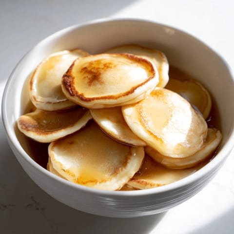 Small, bite-sized fluffy pancake cereal swimming in a bowl of cold, refreshing milk for breakfast.