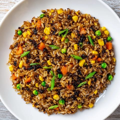 Close-up of umami-rich black garlic fried rice with mixed vegetables, a perfectly cooked egg ribbons, and glistening sesame oil throughout.  