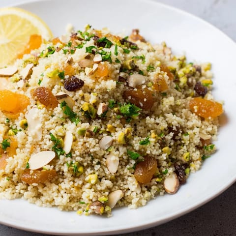 Fluffy couscous pilaf seasoned with warm spices, piled high with almonds, pistachios, and fresh herbs in a serving bowl.  