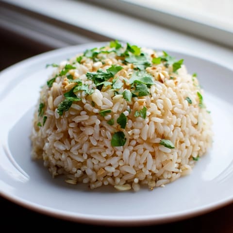 Fluffy jasmine rice with tender garlic bits, steaming gently in a white bowl for a fragrant side dish.  
