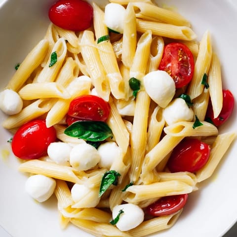 A close-up of Caprese Salad Pasta shows glistening olive oil, torn basil, and bocconcini nestled in short pasta, with balsamic glaze drizzled across.