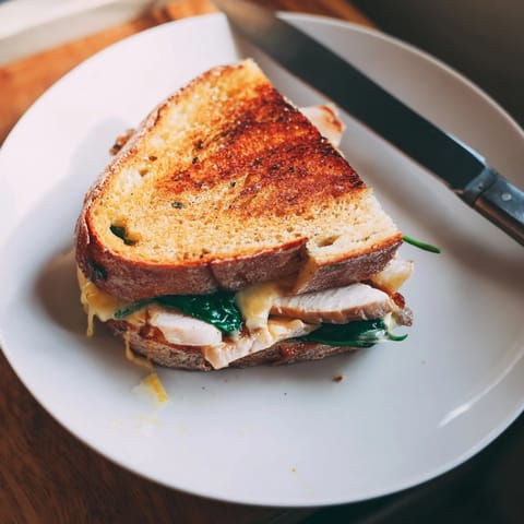 Melty cheese oozes from the warm Grilled Chicken Spinach Panini, served on a wooden board with fresh spinach nearby.