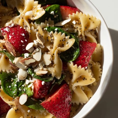 Spring Spinach Strawberry Pasta Salad garnished with crumbled feta, sliced almonds, and basil, served in a white ceramic bowl.