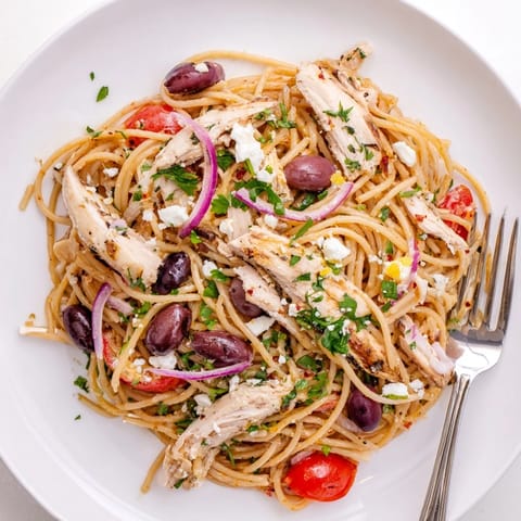 A plate of Greek Chicken Spaghetti topped with crumbled feta, fresh parsley, and a light lemon-herb dressing.