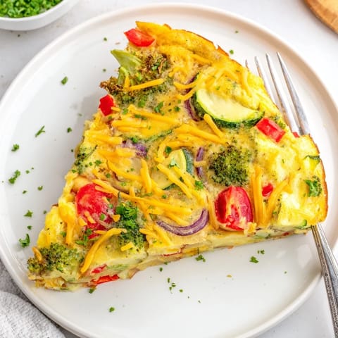 Slice of golden vegetable frittata served on a white plate, garnished with fresh parsley, alongside a simple green salad.  
