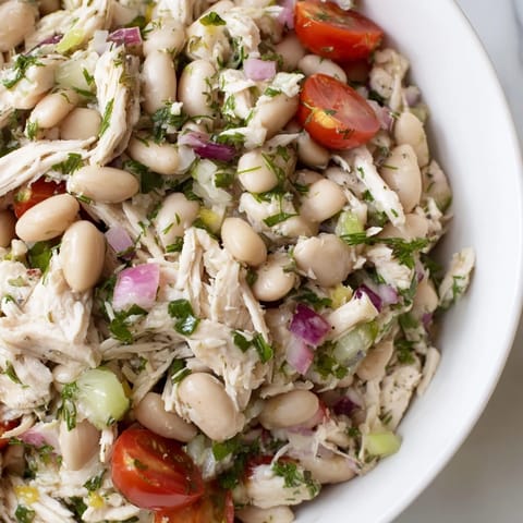 Close-up of Lemony White Bean Chicken Salad featuring fresh dill and parsley, served on a plate with cherry tomatoes and red onion.