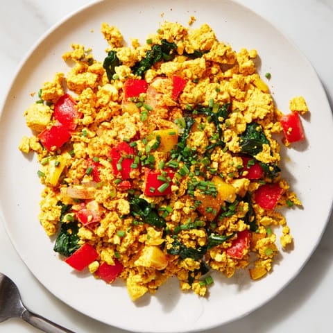 Golden tofu scramble sizzling with diced red bell pepper, onion, and fresh spinach in a skillet, topped with chopped chives and a dash of turmeric for a vibrant, plant-based breakfast.