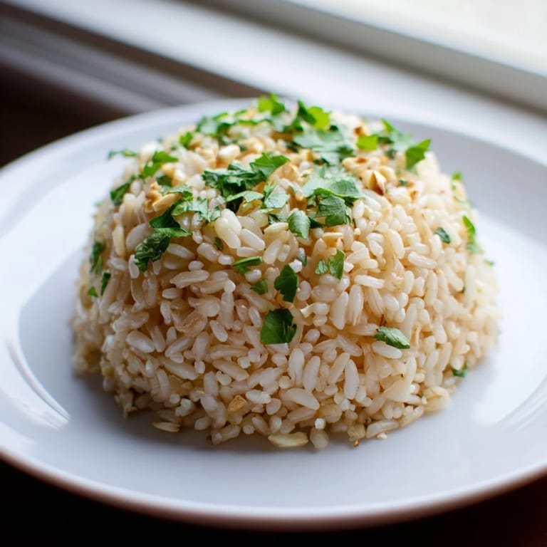 Fluffy jasmine rice with tender garlic bits, steaming gently in a white bowl for a fragrant side dish.  