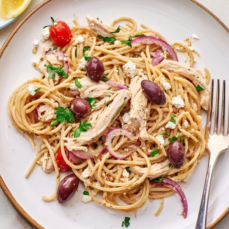 Al dente spaghetti coated in olive oil with juicy chicken, red onion, and colorful tomatoes for an easy Mediterranean dinner.