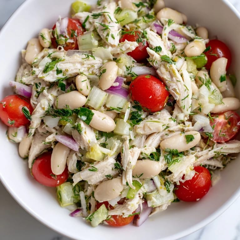 Freshly prepared Lemony White Bean Chicken Salad in a white bowl, garnished with lemon wedges and herbs, perfect for a light lunch.