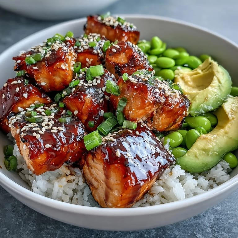 A close-up of marinated salmon atop jasmine rice with edamame, cucumber, and avocado, finished with spicy mayo.