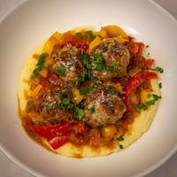 Herb-Cozy Skillet Sausage and Peppers with creamy polenta, a hearty, steaming, Italian-inspired dish on a plate.