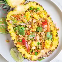 Vibrant Pineapple Fried Rice served inside a hollowed pineapple shell, garnished with cilantro and lime wedges for a tropical Thai-inspired presentation.