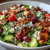 A colorful Greek salad bowl with juicy grilled chicken, fresh veggies, and crumbled feta, drizzled with tangy dressing.